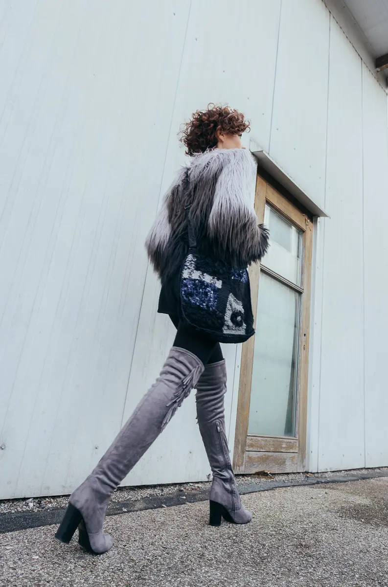Rückansicht im Gehen mit gestrickter Patchwork-Umhängetasche und grauen Overknee-Stiefeln