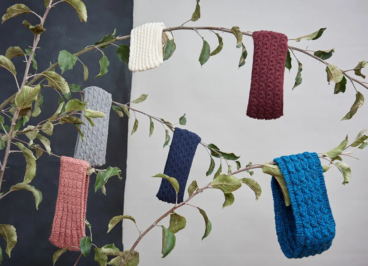Sechs Stirnbänder mit Zopfmuster in Creme, Grau, Altrosa, Bordeaux und Blautönen an Zweigen