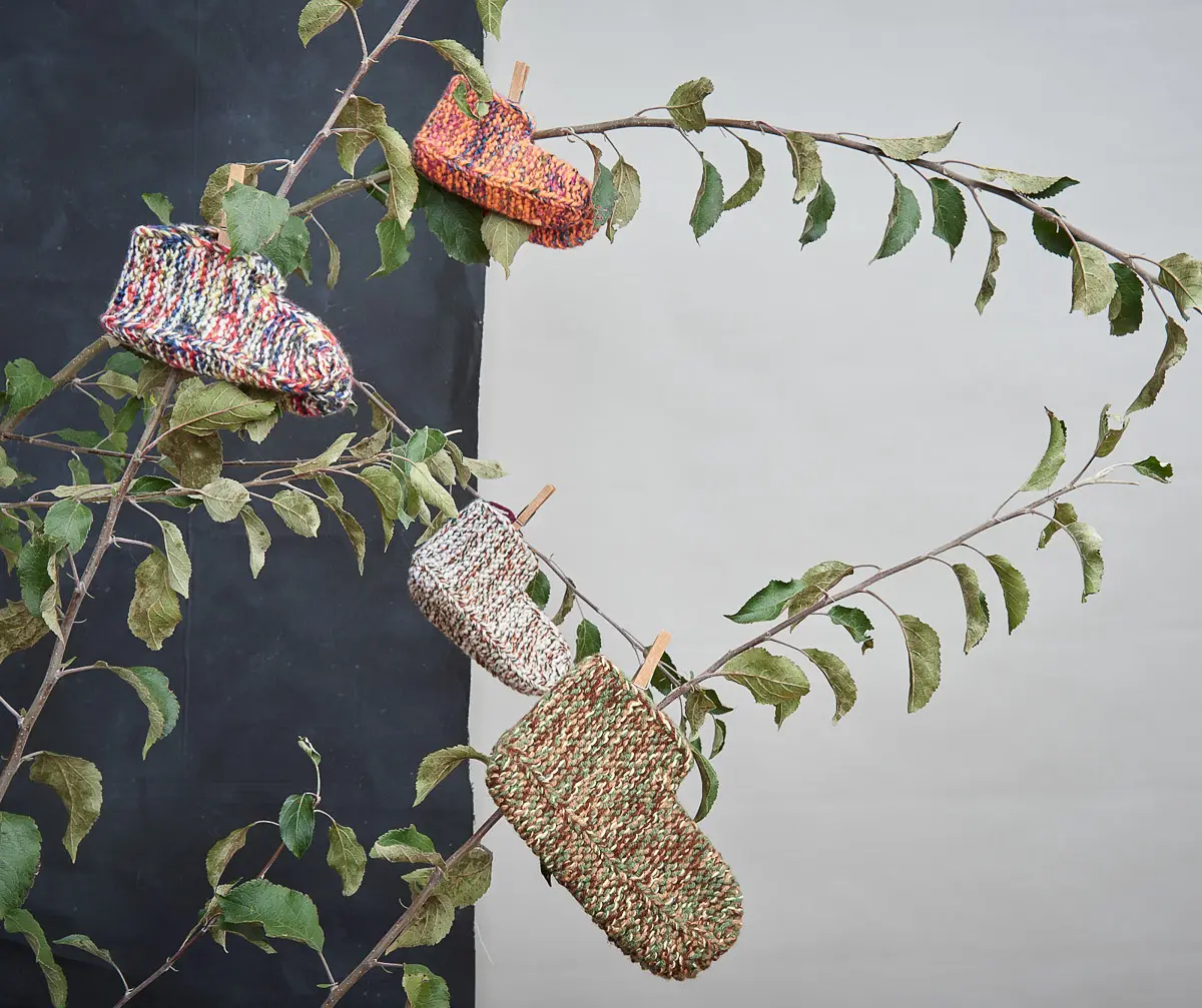 Vier bunt melierte Babyschuhe aus grobem Strick, mit Holzklammern an Ästen befestigt