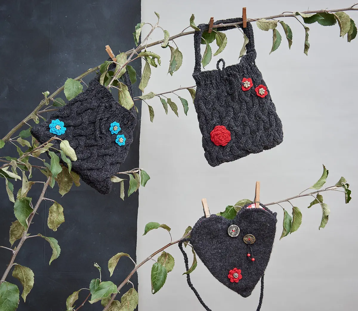 Drei anthrazitfarbene Taschen mit Zopfmuster und gehäkelten Blüten, eine davon herzförmig