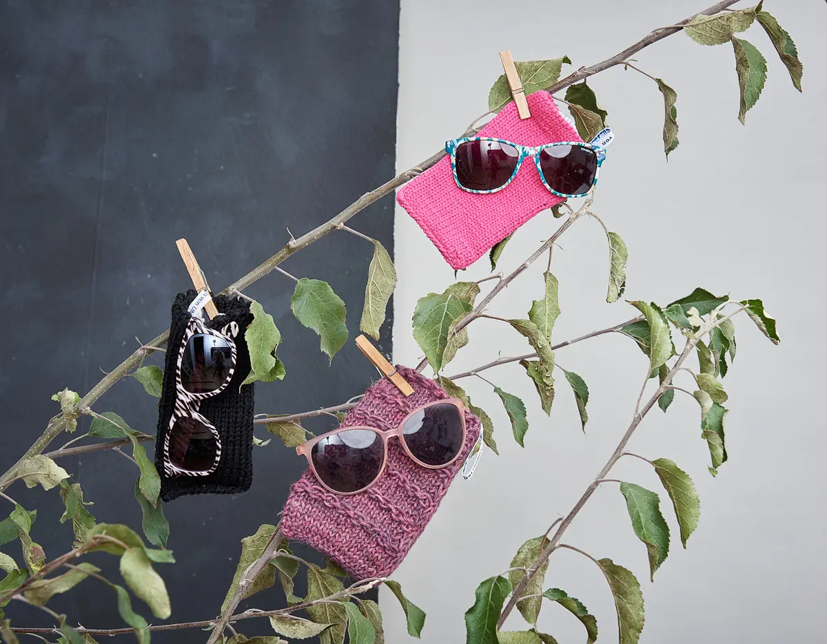 Drei gestrickte Brillenetuis in Pink, Schwarz und Altrosa, mit Sonnenbrillen bestückt und angeklammert