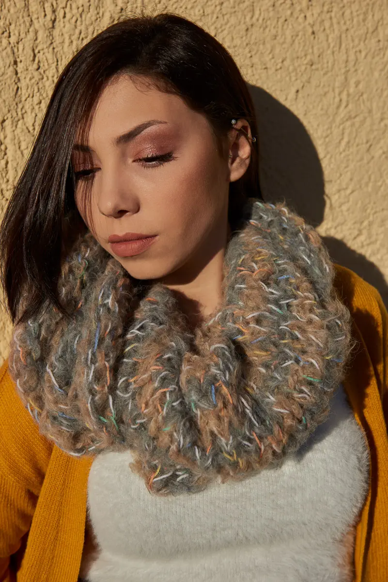 Nahaufnahme eines dick gestrickten Loops in Grau und Beige mit bunten Farbtupfern