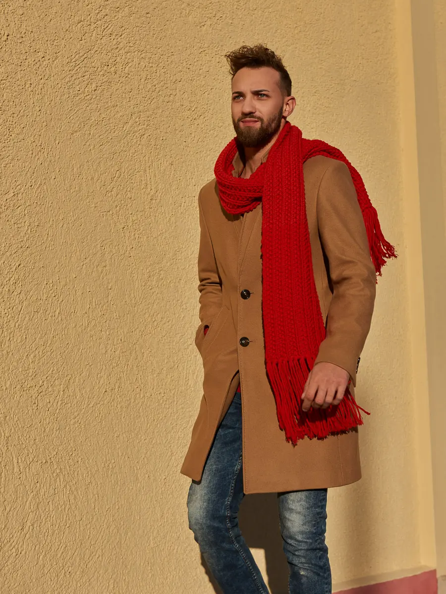 Ganzkörperaufnahme mit leuchtend rotem Rippenschal samt Fransen zu beigem Mantel und Jeans