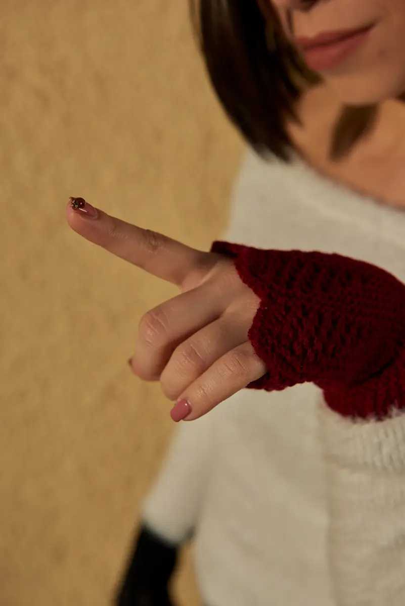 Nahaufnahme einer Hand in dunkelrotem Stulpenhandschuh, auf der Fingerspitze sitzt ein Marienkäfer
