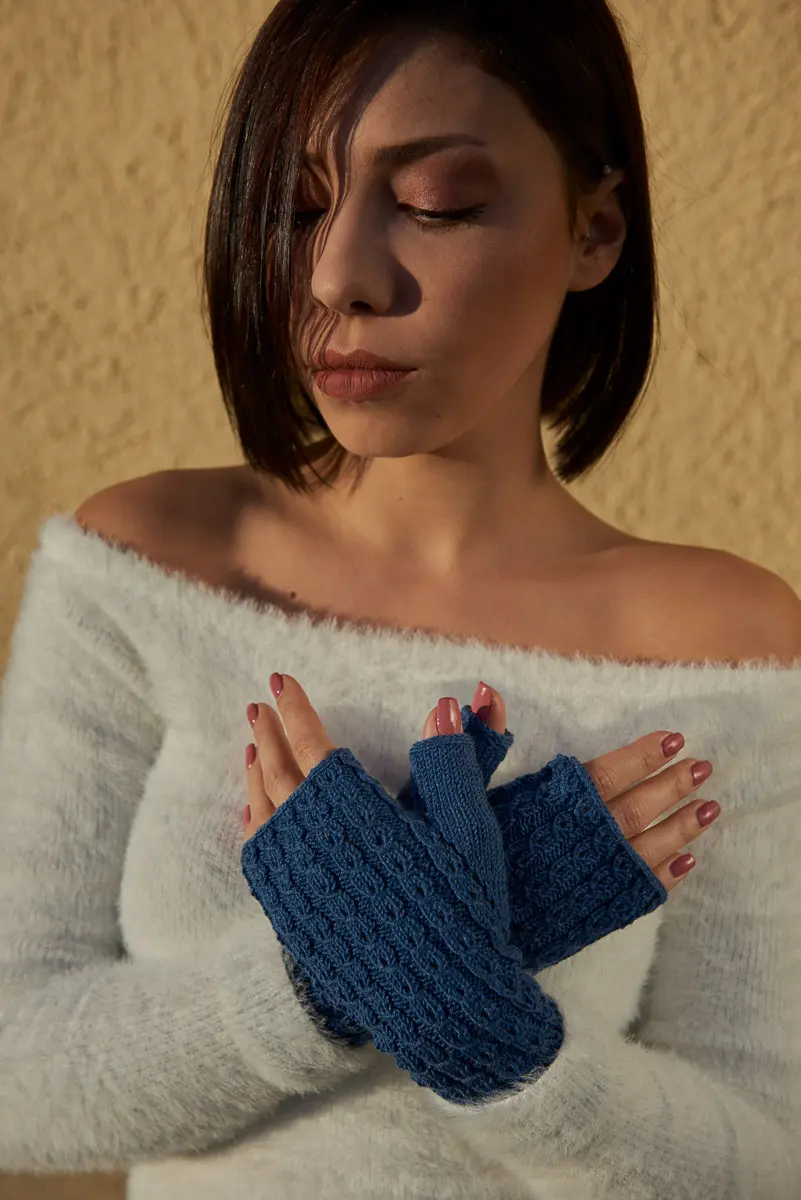 Model im weißen Flauschpullover verschränkt die Hände in blauen Stulpen mit Zopfmuster