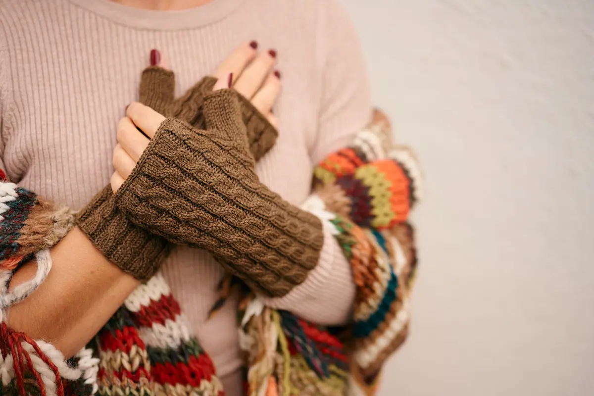 Braune Armstulpen mit Zopfmuster, Arme vor buntem Strickponcho verschränkt
