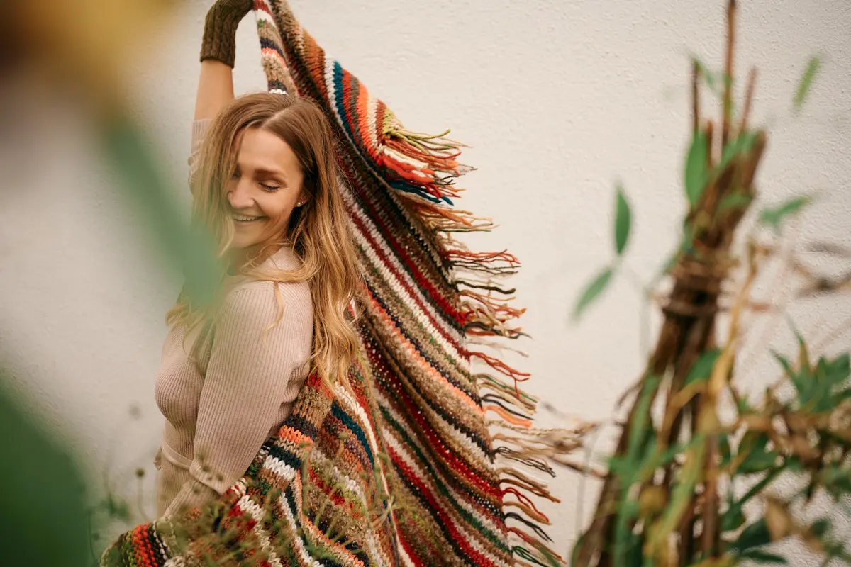 Model schwingt ein großes, bunt gestreiftes Fransentuch schwungvoll durch die Luft