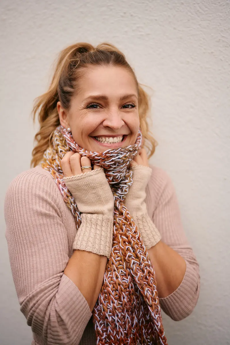 Lachendes Model mit dick gestricktem Schal in Rost und Weiß vor heller Hauswand