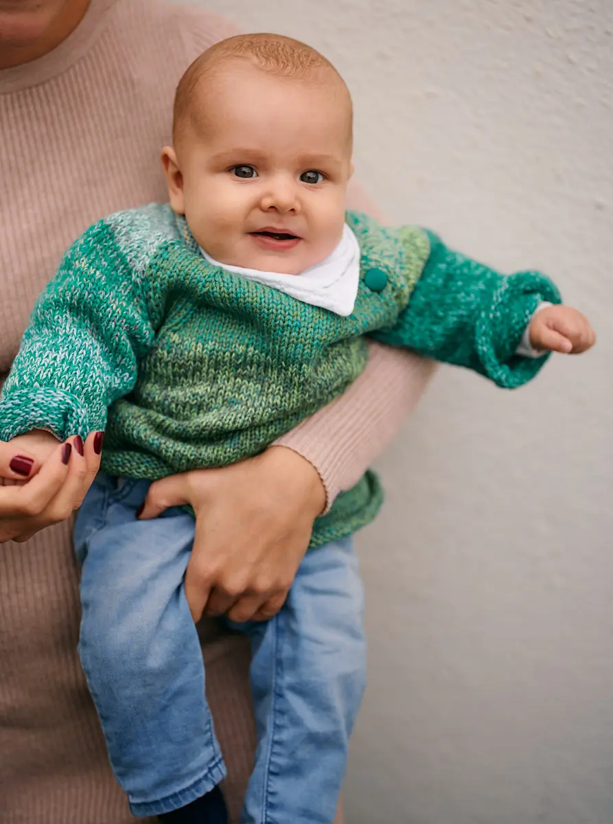 Kind im grün melierten Strickpullover mit Knopf am Kragen, auf dem Arm gehalten